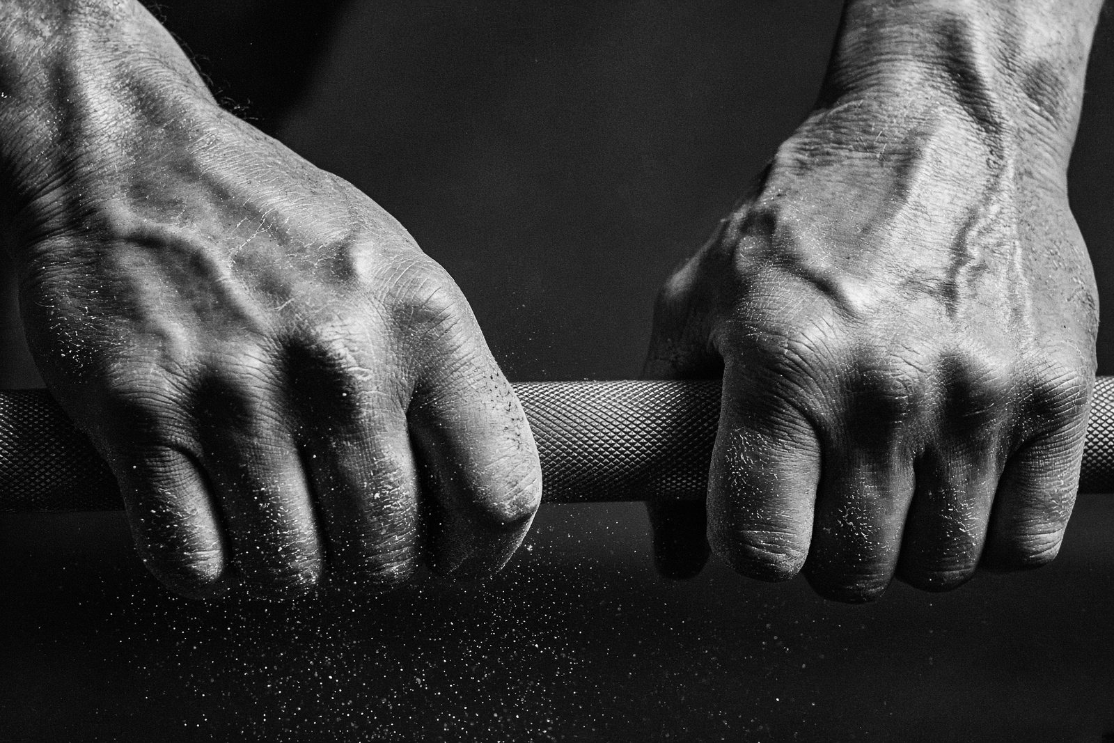 Chalked hands gripping a knurled barbell in high-contrast black and white.
