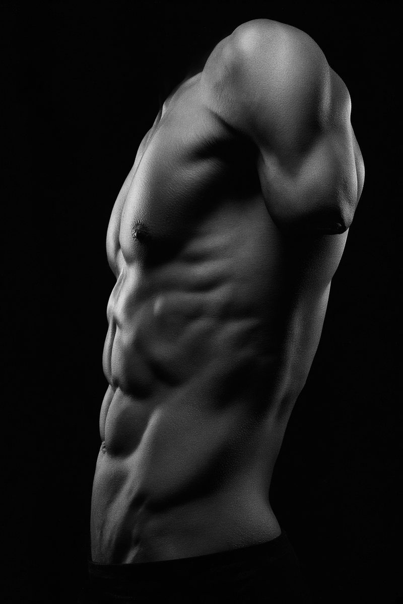 Black-and-white studio photograph of a developed physique, waist to shoulder.